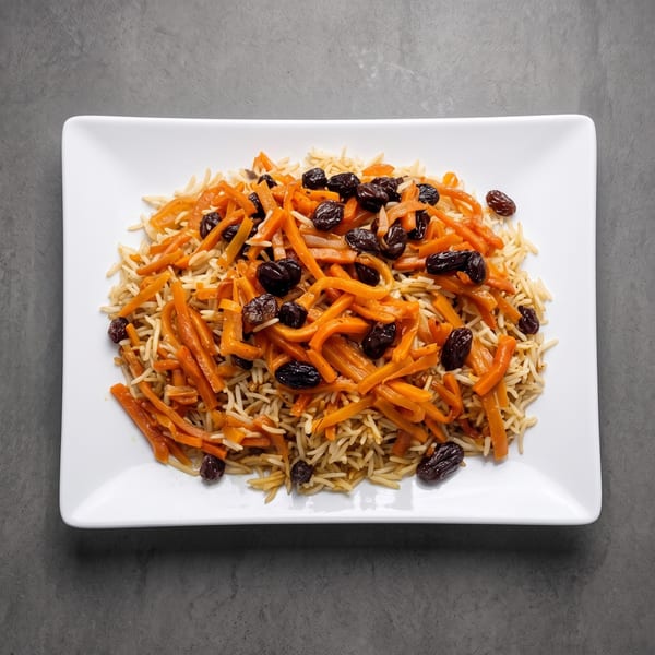 Golden rice topped with julienned carrots and dark raisins on a white plate.
