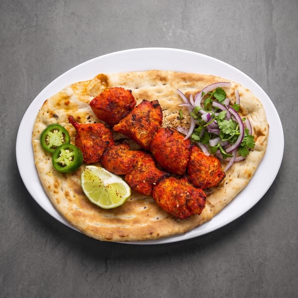 Spicy red chicken tikka on naan with lime, green chilies, red onion, and cilantro.