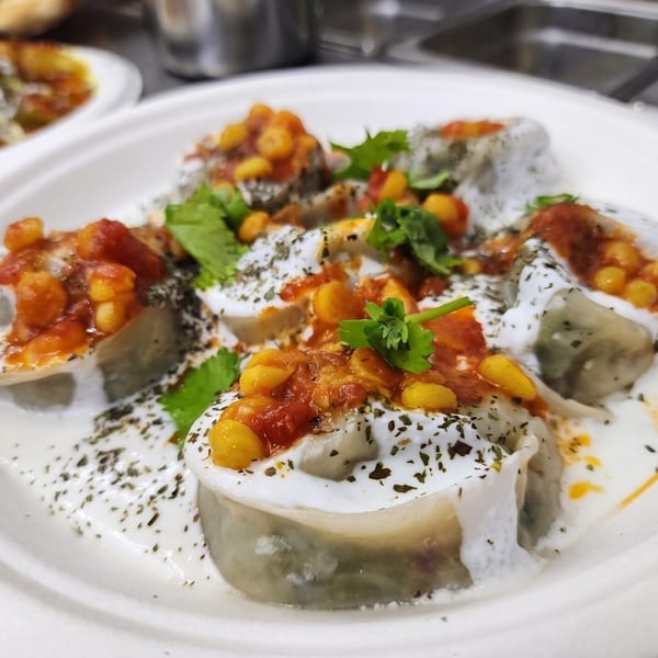 Plate of dumplings topped with creamy sauce, spicy red sauce, yellow kernels, and fresh herbs.
